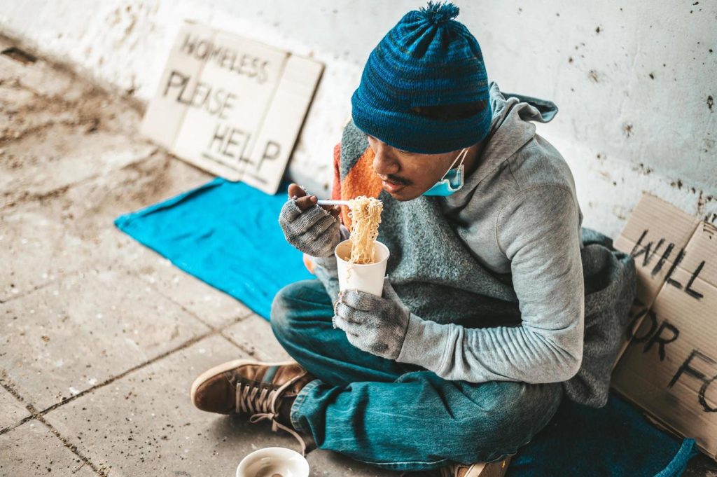 homeless-man-wrapped-in-cloth-and-eating-noodles-free-photo